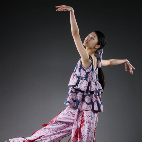 model in a flowery garment with a frilly top and pink frilly and flowery bottoms - posing in front of a grey background