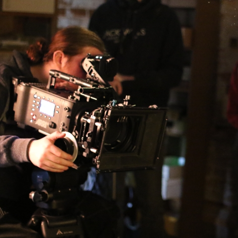 Image of a student behind a camera pointing the camera towards a clapperboard 