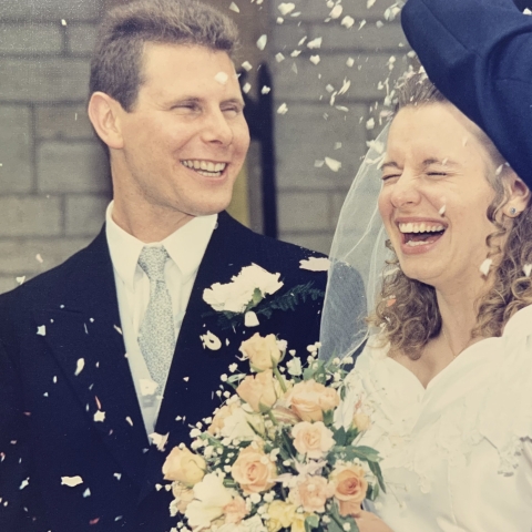 an image from a wedding there is a groom on the left and a bride on the left there is a bouqet in the middle. confetti can be seen falling