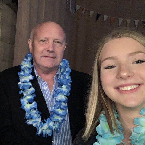 A selfie photo of Erin and her Grandad. They are both smiling at the camera and are wearing a Hawaiian flower garland around their necks. 