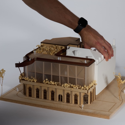 An architectural model with a hand adjusting a component on a detailed building form.