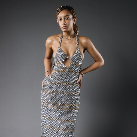 Image of model wearing a garment that is a long silver dress and in front of a grey background