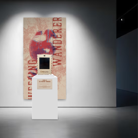 Gallery installation featuring a pedestal with a small digital device labelled “Entropia” in front of a large red‑and‑blue anatomical heart artwork titled “Weeping Wanderer.”