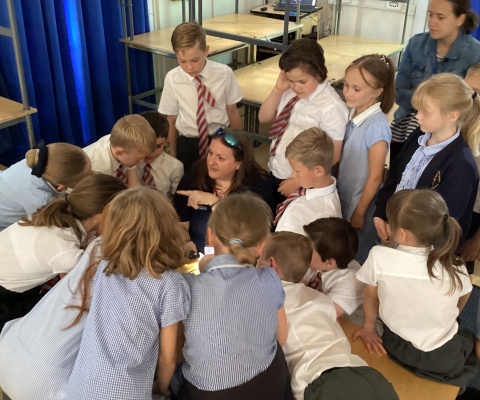 Dr Fay Couceiro looking through a microscope surrounded by children