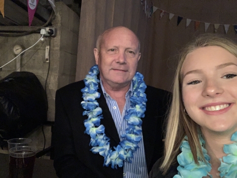 A selfie photo of Erin and her Grandad. They are both smiling at the camera and are wearing a Hawaiian flower garland around their necks. 