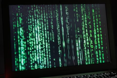 A close-up of a computer screen in a dark room with lots of green numbers, letters and symbols on a black background