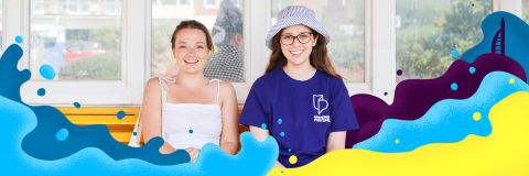Two students sat at the beach, one wears a hat and a University of Portsmouth tshirt, it is Clearing