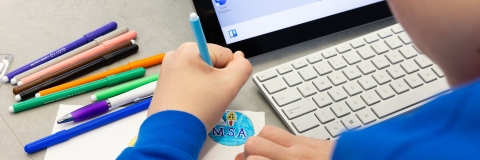 A school pupil working on a drawing with coloured pens, with a laptop in the background