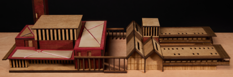 A tall rectangular tower sits beside a larger block‑shaped building with red accents and flat roofs, both made from wood and cardboard.
