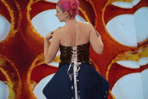 model wearing blue garment whilst facing away from camera. They are posing whilst standing infront of an LED screen