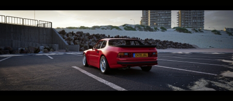 A Computer generated red Porsche win a car park in a snowy setting with buildings in the background. Our view is of the rear of the car
