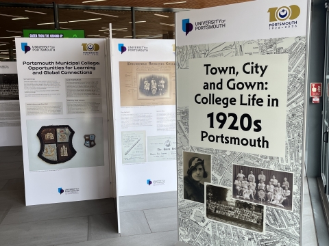 A view of the exhibition 'Town, City and Gown' with large display boards in an open area. The board at the front reads 'Town, City and Gown: College Life in 1920's Portsmouth