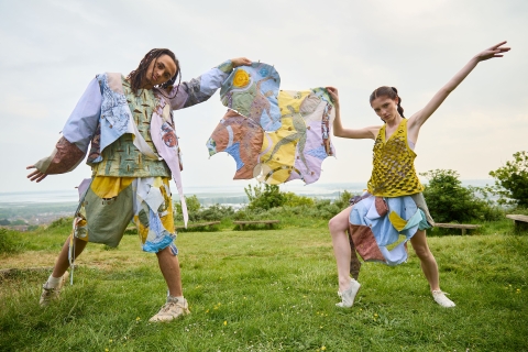 The models posing on a grassy area whilst holding some fabric/material between them