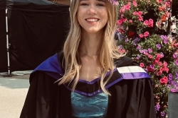 Girl with blonde wavy hair smiling in a graduation gown