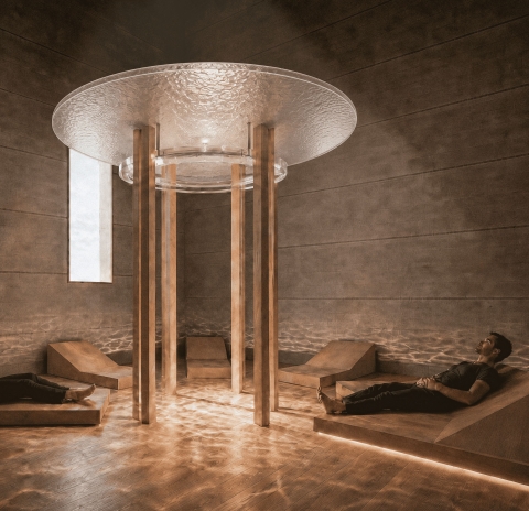 A circular interior space with a reflective ceiling feature, supported by columns, with people reclining on lounge chairs around the room.