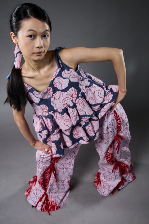 Model wearing full costume including pink/red trousers and a darker pink/blue top.
