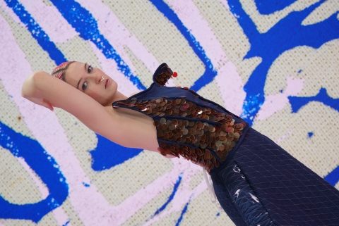 student wearing blue garment whilst in front of an LED screen. the student is leaning backwards and posing