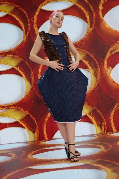 Model with pink hair wearing a blue garment whilst standing on an LED stage 