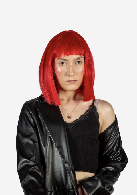 A close‑up black‑and‑white image showing part of a person with straight, bright red hair cut into a blunt bob with bangs. They wear a black leather jacket draped off one shoulder, a black lace‑trimmed camisole, and a small pendant necklace, set against a plain white background.