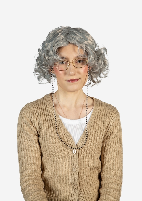 A person wearing a curly grey wig, glasses with a chain, a beige ribbed cardigan, and a white top, shown against a plain white background.