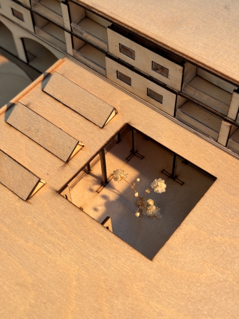 A cardboard architectural model of a multi‑storey building with a cut‑out roof revealing a small planted courtyard inside.
