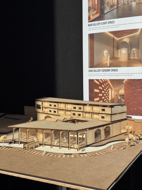 A wooden architectural model with angular forms, an opening slanted roof, and small figures, shown in front of a poster labeled “Sensory Space.”