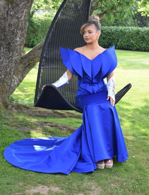Student wearing bright blue garment with large shoulder pads whilst sitting on a swinging chair hanging from a tree
