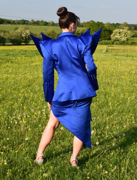 Student with black hair wearing bright blue garment - facing away from the camera whilst in a grassy area