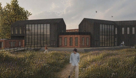 A modern building with two dark glass volumes and a reddish central entrance, set in a grassy field with a dirt path and a few people walking nearby.