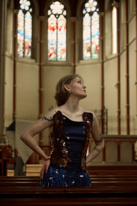 student posing in what looks like a church surrounded by colourful glass windows. student is wearing blue garment