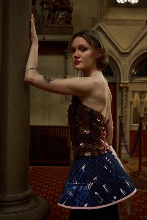Model posing in what looks like a church wearing a fashion garment - the model is posing whilst leaning on a structure within the church