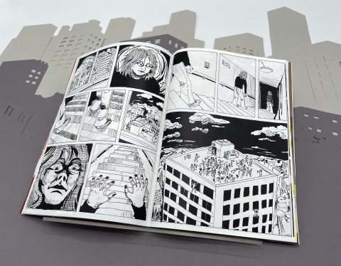 An open black‑and‑white comic book showing panels of a long‑haired character in tense scenes on the left page, and on the right a hallway scene and a rooftop crowd, all set against a stylised paper cityscape backdrop.