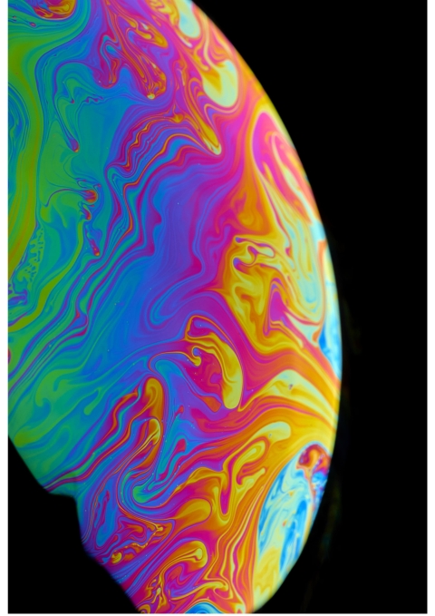 A close‑up of vivid swirling blue, pink, yellow, orange, and green patterns on a soap‑bubble surface against a black background.