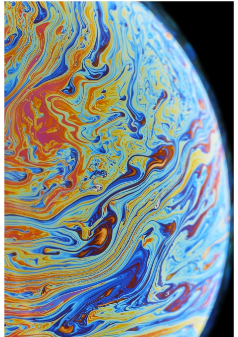 A close‑up of swirling blue, orange, yellow, and purple patterns on a soap‑bubble surface, forming a vivid marbled abstract.