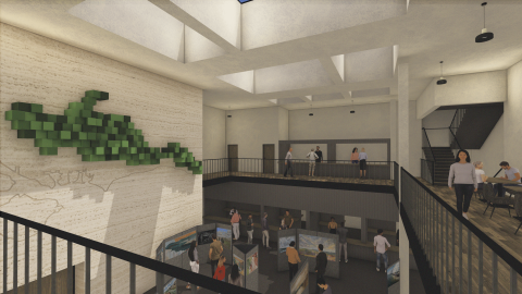 Two‑storey gallery space with a central staircase, people viewing displays on both levels, and a large green geometric wall sculpture.