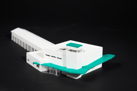 A white architectural model with green roof sections, showing a multi‑level building with a tower, arched openings, and interconnected blocks.